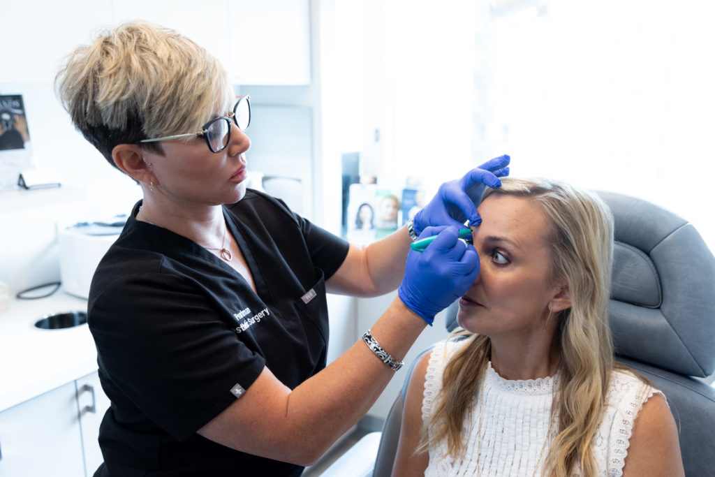 woman in scrubs marking patient's forehead