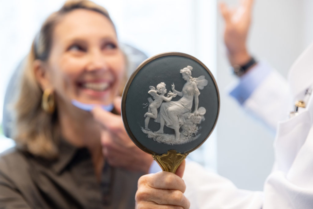 Dr. Pearlman using chin implant tool on woman's smiling face with mirror