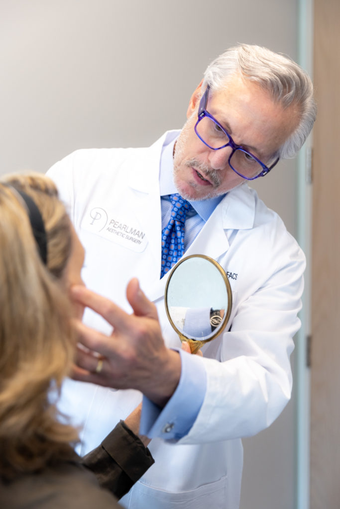 Dr. Pearlman looking at woman's face with mirror