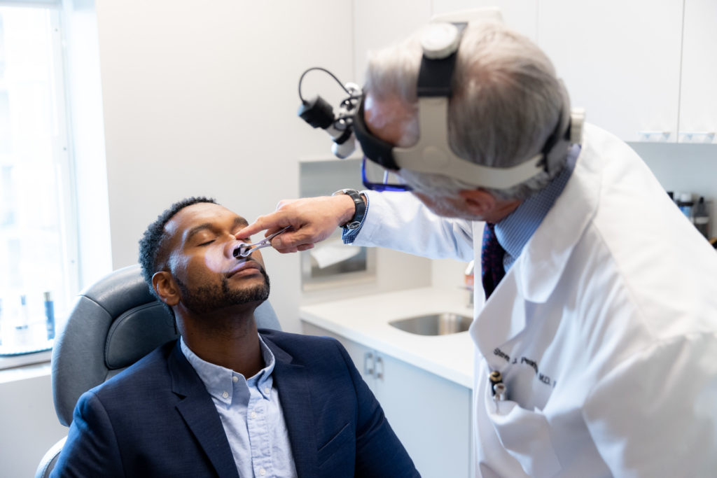 Dr. Pearlman using tool to look at patient's nose for rhinoplasty consultation