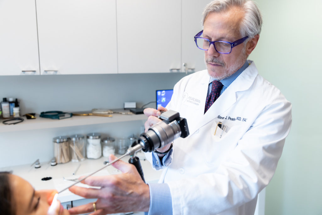 Dr. Pearlman looking at patient's nose with tool during rhinoplasty consultation