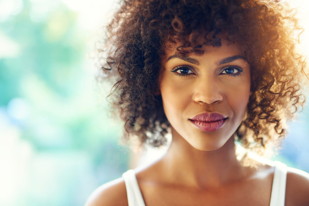 curly haired woman with white top and blurred background