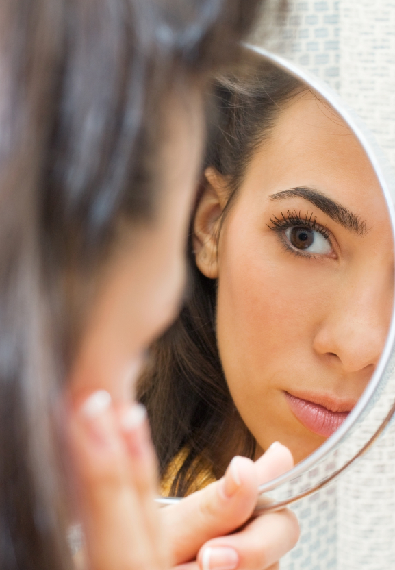 over the shoulder image of woman examining face in mirror