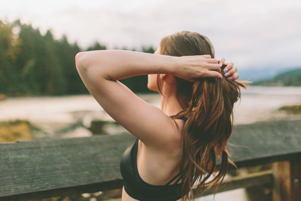 woman in sports bra fixing hair outside