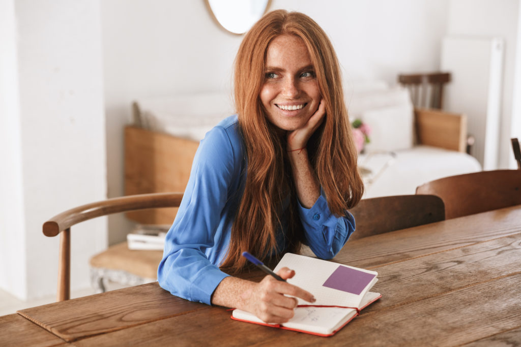 red haired woman writing in journal and smiling